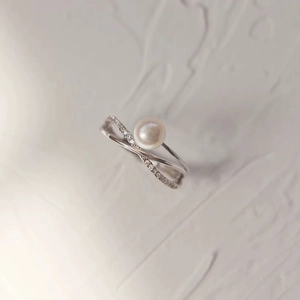 Macro detail of cross-band pearl ring with cubic zirconia inlay on elegant gray texture