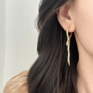 Elegant gold snake earrings with white zircons and green eyes worn by a model