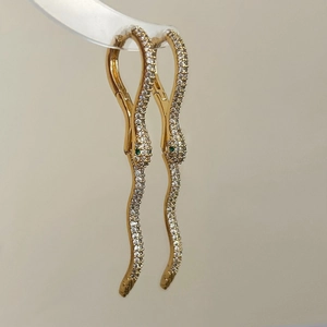 Detail of gold snake earrings with sparkling white zircons and green gemstone eyes