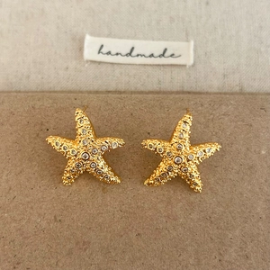 Détail de boucles d'oreilles étoile de mer dorées avec zircons sur support fait main