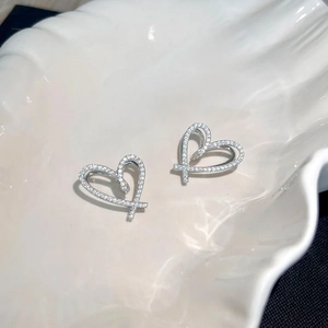 Elegant silver heart stud earrings with pavé cubic zirconia on a white shell tray