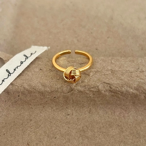 Close-up of golden knotted adjustable ring on rustic background with handmade ribbon