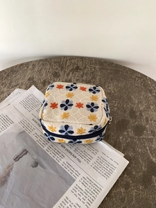 Close-up of floral embroidery on a linen makeup bag placed on a rustic wooden table