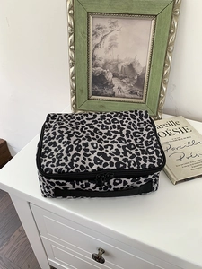 Grote toilettas met luipaardprint, dubbele ritsen en handvatten op een witte kast