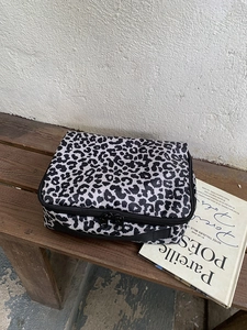 Detail van luipaardprint make-up tas met zwart handvat en rits op een houten krukje
