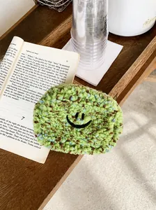 Nahaufnahme der grünen Plüsch-Mini-Geldbörse mit Smiley-Stickerei auf einem offenen Buch