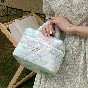 Quilted floral makeup bag with dual zippers and handle shown in an outdoor setting