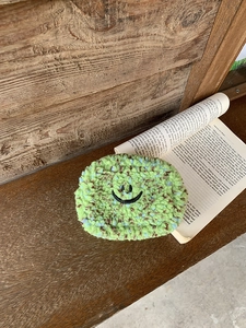 Detail einer süßen Teddy-Vlies-Minitasche mit besticktem Smiley auf einer Holzbank