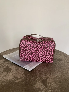 Detail van roze make-uptas met luipaardprint, ritssluiting en handvat op hout