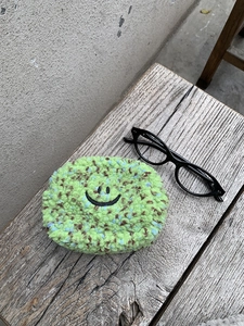 Nahaufnahme der grünen Plüsch-Mini-Tasche mit Punkten und Smiley auf Holzoberfläche