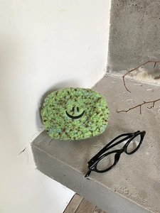 Detailansicht einer weichen grünen Plüsch-Mini-Kosmetiktasche mit Smiley-Stickerei