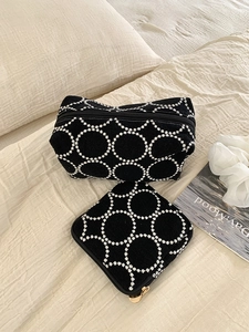 Détail de l'ensemble de trousses de maquillage brodées noir et blanc sur tissu beige