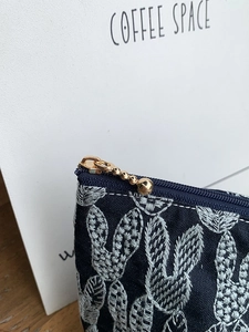 Detail of silver leaf embroidery on navy fabric bag with golden bead chain zipper pull