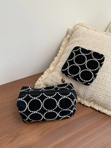 Détail de grandes trousses à maquillage en toile noire avec broderies circulaires blanches