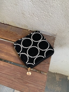 Trousse à maquillage noire brodée avec motif floral blanc et zip doré sur un banc en bois
