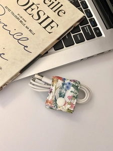 Floral fabric cable organizer with snap button holding a white USB cord on a desk