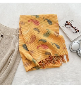 Detail of yellow paisley scarf with fringe edges and knit texture on a white background