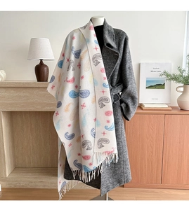 Close-up of beige paisley scarf with star patterns and white tassels on a grey coat