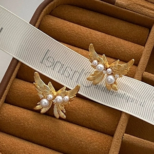 Boucles d'oreilles papillon dorées avec perles et strass sur un coffret en velours