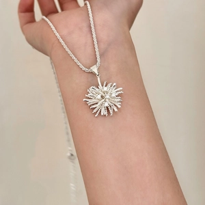 Close-up of a silver zircon firework pendant necklace worn on neck for size reference