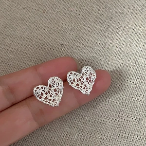 Pair of hollow lace-patterned heart stud earrings in silver finish held by hand