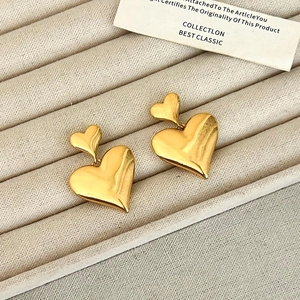 Close-up of double gold heart stud earrings on a beige velvet jewelry display tray