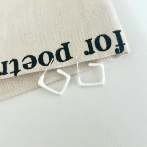Detail view of white square geometric earrings on beige canvas textured background