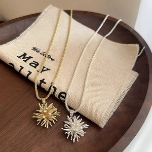 Elegant gold and silver firework pendant necklaces with cubic zirconia on beige linen