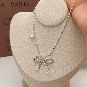 Silver bow necklace with olive beads and white pearls on a minimalist display stand