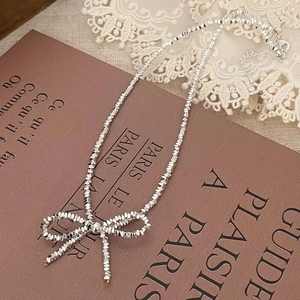 Silver bow necklace featuring faceted metal beads on a vintage French book and lace