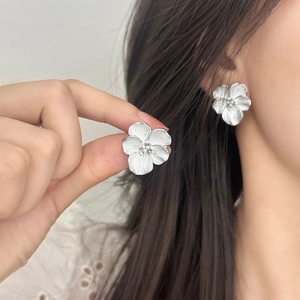 Elegant silver flower stud earrings with brushed texture and petal detail on a model