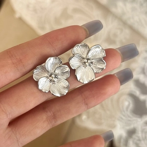 Detailed close-up of a silver floral stud earring with textured petals and center beads