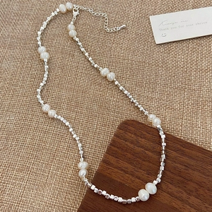 Dettaglio della collana di perle bianche e perle quadrate d'argento su sfondo di tessuto