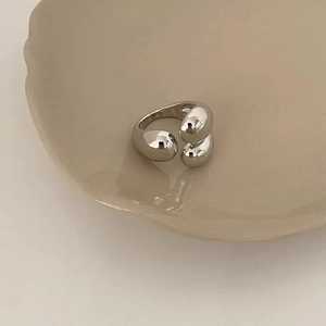 Detail view of silver triple water-drop rings on a ceramic plate with minimalist design