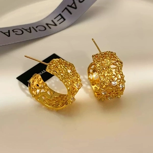 Detail of gold hollow lace earrings with sparkling cubic zirconia on a warm background