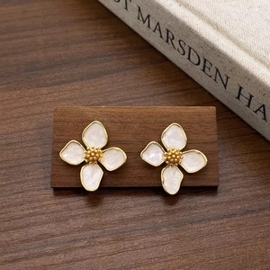 Détail de boucles d'oreilles fleurs en émail blanc et finition dorée sur socle en bois