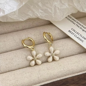 Gros plan de boucles d'oreilles créoles dorées avec pendentifs fleurs blanches à cinq pétales