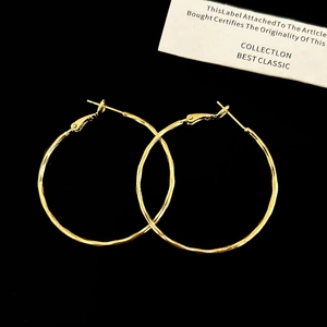 Macro detail of gold-tone hoop earrings with a handcrafted hammered texture on black background