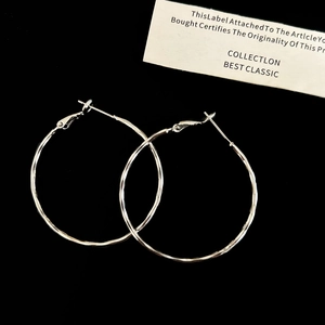 Macro shot of silver-toned hoop earrings featuring a textured hammered finish on black