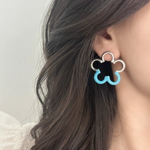 Minimalist silver and blue flower stud earrings with hollow cut-out design on a model