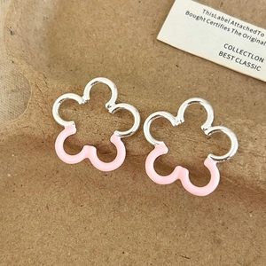 Close-up of silver flower stud earrings with pink enamel coating on textured paper
