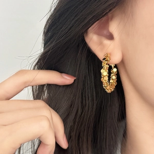 Fashionable gold hoop earrings with textured sequin design worn by a model