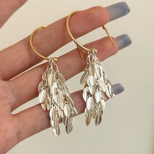 Detail of silver leaf fringe earrings held by hand showing multi-layer metallic tassel design