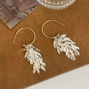 Detail of layered silver leaf fringe earrings with golden hoop hooks on a wood background
