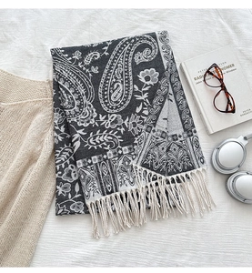 Detail of paisley pattern shawl with white tassels next to a book and glasses