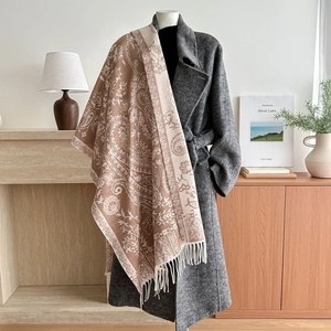 Beige paisley jacquard shawl with tassels over a grey coat in a cozy home setting