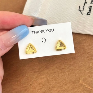 Macro view of gold triangle stud earrings with textured finish and micro-bead edges