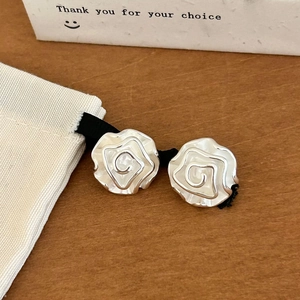 Close-up of silver rose stud earrings with spiral design on warm wood surface