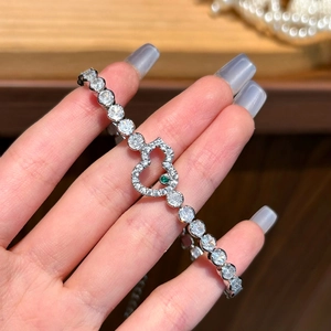 Silver heart bracelet with green gemstone and white zircon stones on a wooden background