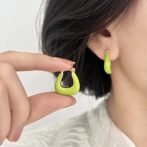 Élégantes boucles d'oreilles en émail vert en forme de U dorées portées par un mannequin